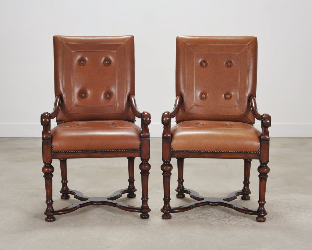 A pair of classic wooden armchairs with tan leather tufted seats and backs.