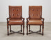 A pair of classic wooden armchairs with tan leather tufted seats and backs.